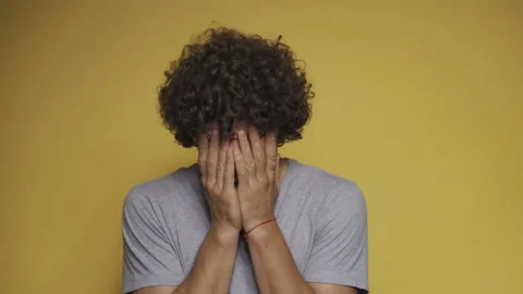 Curly-haired guy sobs with his hands covering his face. Man cries in the studio Stock Footage 139464791