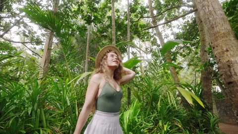 Curly-haired lady in straw hat admires lush garden greenery. Wanderer explores Stock Footage 264866429