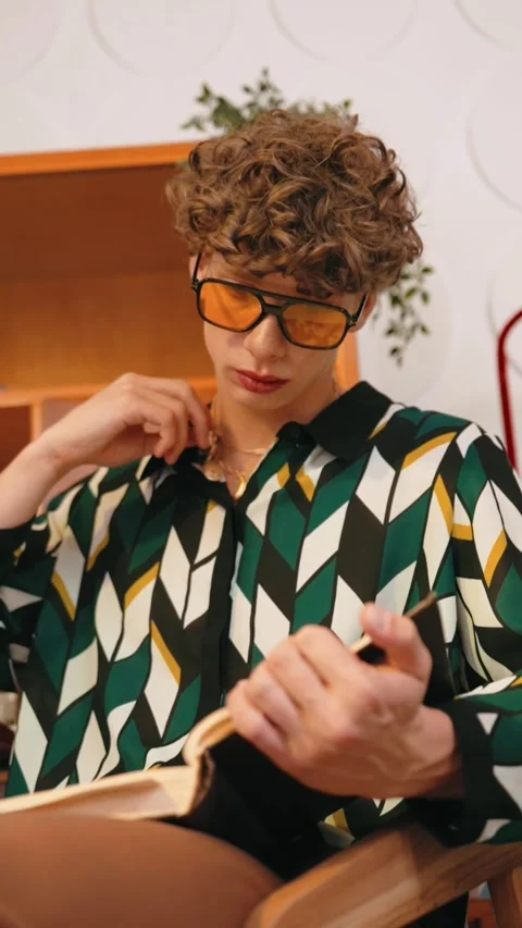 Curly-haired man in patterned shirt and orange glasses reading book Stock Footage 299821128