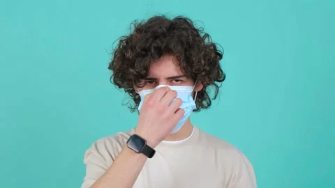 Curly haired man puts a mask on his face from air pollution and coronavirus. 스톡 동영상 150960154