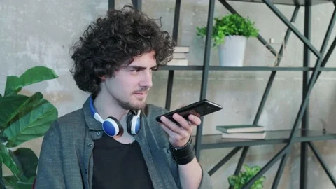 Curly haired man sit at desk at home office and talk on loudspeaker on Stock Footage 155807167