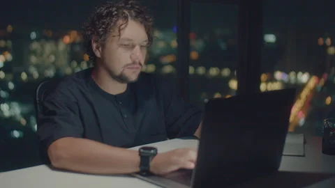 А curly-haired man works at a computer at night Stock Footage 240279877