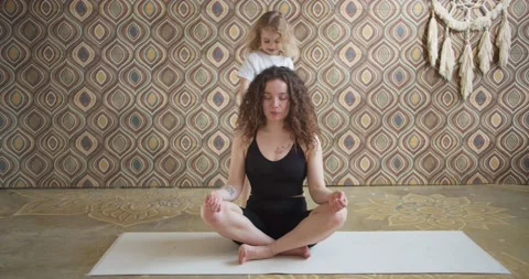 Curly-haired mother meditates while sitting on a yoga mat, while active Stock Footage 153174356