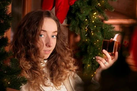 The curly haired person smiles while presenting a wrapped present near evergr Stock Photos