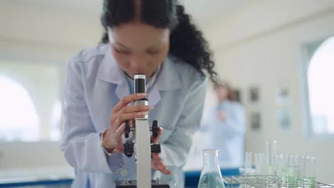 Curly-haired scientist peers through microscope in lab Stock Footage 340448665