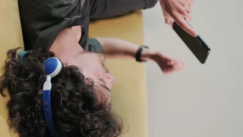 Curly haired young man on the couch listening music with headphones. Stock Footage 155403846