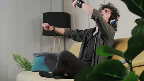 Curly haired young man on the couch listening music with headphones. Stock Footage 156329572