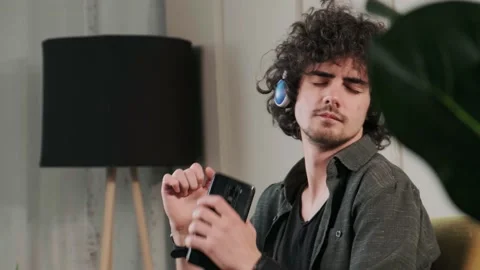 Curly haired young man on the couch listening music with headphones. Stock Footage 168531432