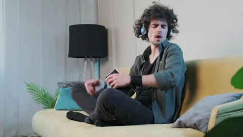 Curly haired young man on the couch listening music with headphones. Stock Footage 169399546