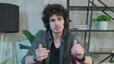 Curly haired young man looking at camera and talking using a headphones. Stock Footage 155807120