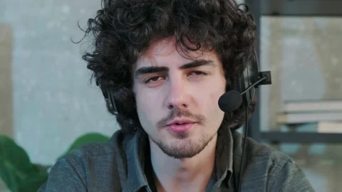 Curly haired young man looking at camera and talking using a headphones. Stock Footage 168531332