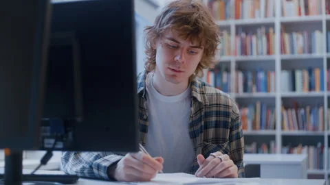 Curly-Haired Young Man Working on Assignment at Computer in Academic Library 스톡 동영상 335123995