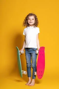 Curly happy girl in white polo, blue jeans and holding two colorful skateboards Stock Photos