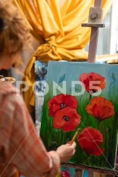 Curly red-haired artist standing near canvas with red poppies Stock Photos