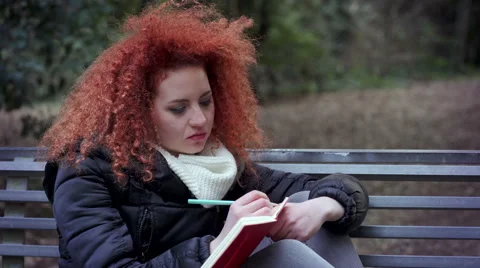 Curly redhead girl on a bench writes her diary 스톡 동영상 59343122