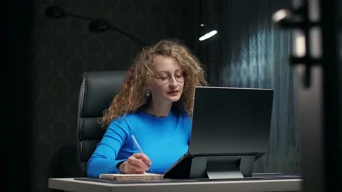 Curly woman learning online using laptop and notepad sitting at home.Young girl Stock Footage 232132293