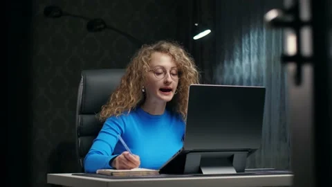 Curly woman learning online using laptop and notepad sitting at home.Young girl Stock Footage 232162654