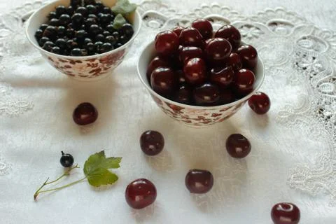Currant berries and cherries on a white plate and white tablecloth Stock Photos