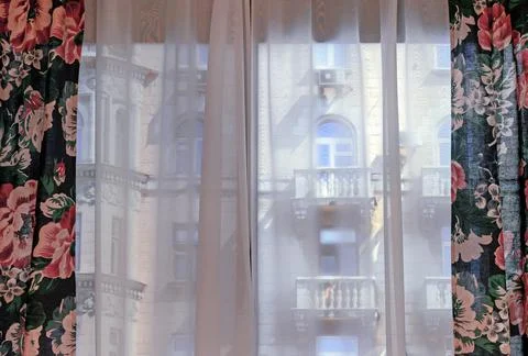 Curtains with floral patterns on the window overlooking the old building. Stock Photos