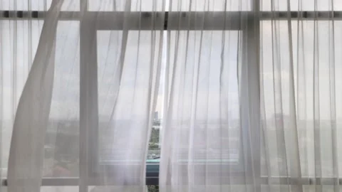 Curtains flutter in the wind from an open window in a wall of square windows Stock Footage