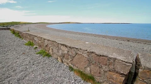 Curve of wall, pebble beach and sea, blue sky. Stock Footage 281253745