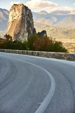 Curved asphalt mountain road with stone safety wall leading toward monolithic Foto stock