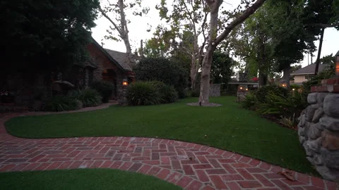 Curved brick path and lawn in front of a stone house at dusk Stock Footage 345529666