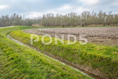 Curved ditch along a plowed field in the autumn season Stock Photos