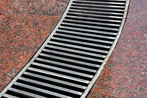 Curved drainage system with stripes grate on the granite floor. Stock Photos