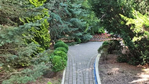 Curved garden walkway bordered by evergreen trees, trimmed shrubs, mulch beds Video stock 343514882