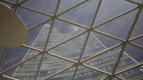 Curved glass skyscraper seen through modern geometric roof structure blending ar Stock Footage 312602889