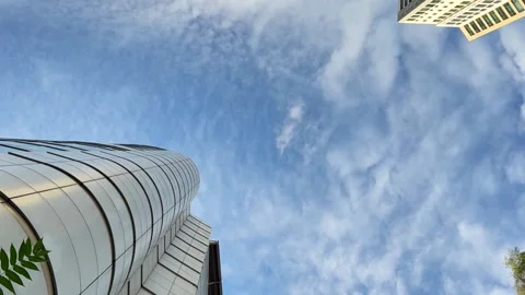 Curved glass skyscraper viewed from low angle against blue sky with clouds Stock Footage 337104386