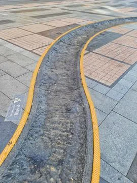 Curved gray concrete gutter bordered by vibrant yellow trim flows across a st Stockfoto's