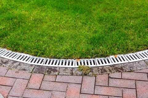 Curved iron grid drainage system in the park by the green lawn and footpath. Stock Photos