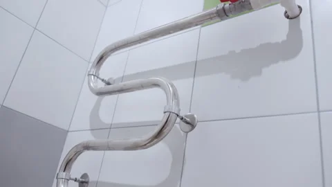Curved metal radiator pipe features valves in tiled bathroom Stock Footage 335644302
