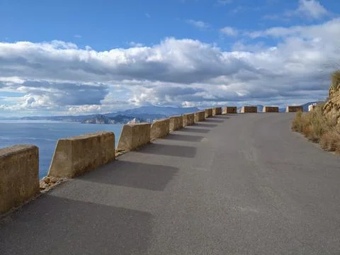 Curved oceanfront highway featuring stone barriers and dramatic cloud forma.. 库存照片