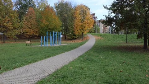 Curved pedestrian path through green park with blue outdoor gym and benches surr Video stock 319841942