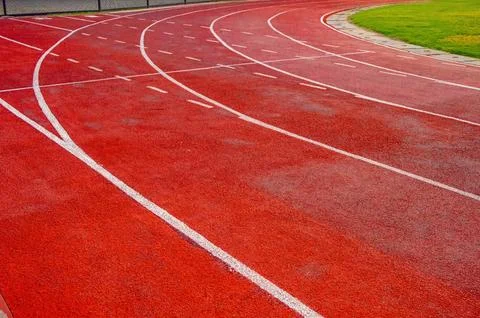 Curved red running track with dashed white lane lines beside grass and fenc.. Stock Photos