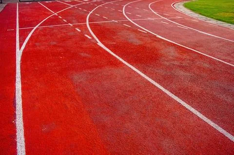 Curved red running track with dashed white lane lines beside grassy field, .. Stock Photos