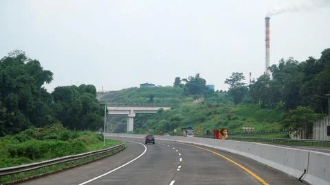 The curved road of the Trans Java Toll Road during the day, factory chimney.. Stock Photos