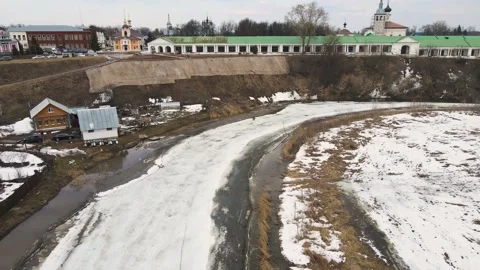 A curved small frozen river, the ice is melting, there is a town on the bank. Stock Footage 225836364