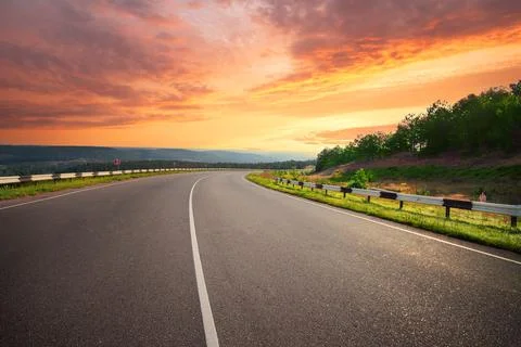 Curving asphalt road under dramatic sunset sky Stock Photos