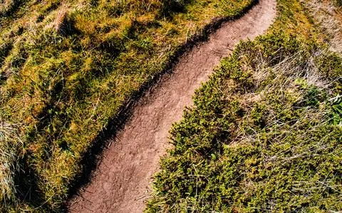 Curving dirt path through grassy hills with blue sky overhead Stock Photos