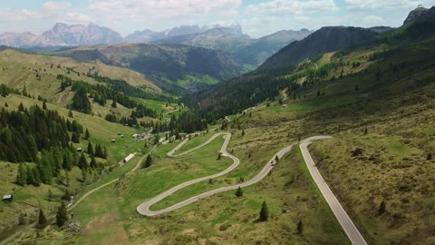 Curving mountain road crossing an alpine valley with forests and rocky peaks 動画素材 337079148