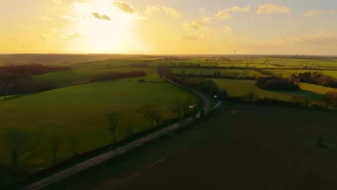 Curving road stretching through rolling green fields under golden evening light Stock Footage 311437116