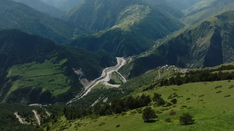 Curvy mountain roads cutting through lush green hillsides, leading to a small Stock Footage 265560189