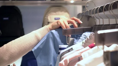 A customer carefully looks through the T-shirts hanging on hangers in a store Stock Footage 276458804