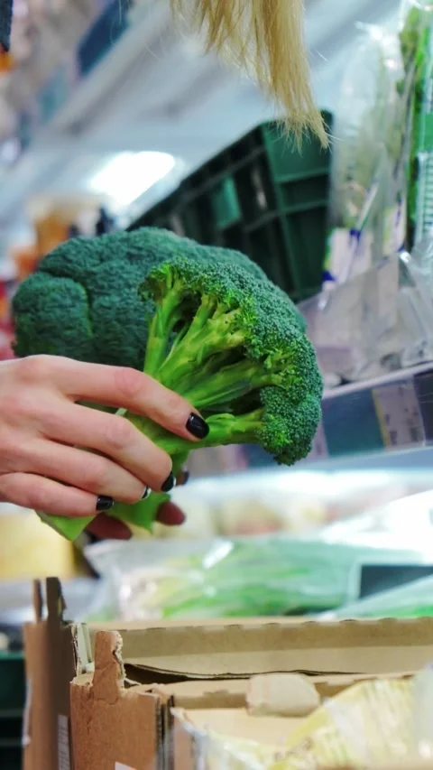Customer chooses fresh green broccoli from grocery store shelf while shopping Stock Footage 346774409