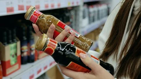 Customer comparing two sauce bottles in a supermarket and making a decision Stock Photos