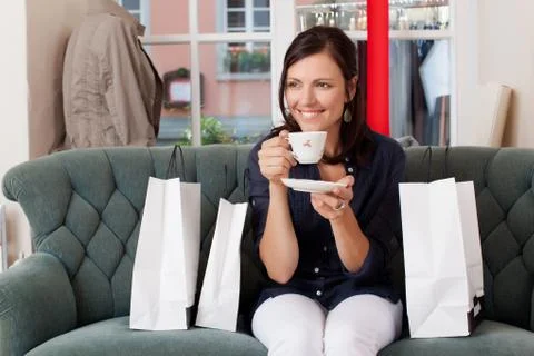 Customer drinking coffee while sitting on sofa at clothing store Stock Photos